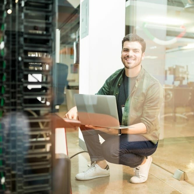 portrait-happy-young-male-network-engineer-with-laptop-hand-working-datacenter